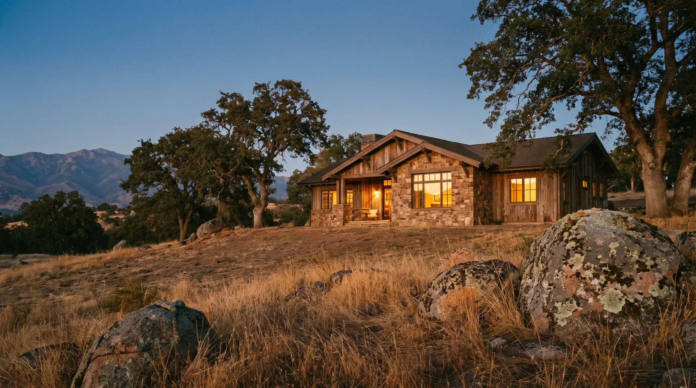 A Northern California foothill home at dusk, oaks and granite outcrops on golden hillside